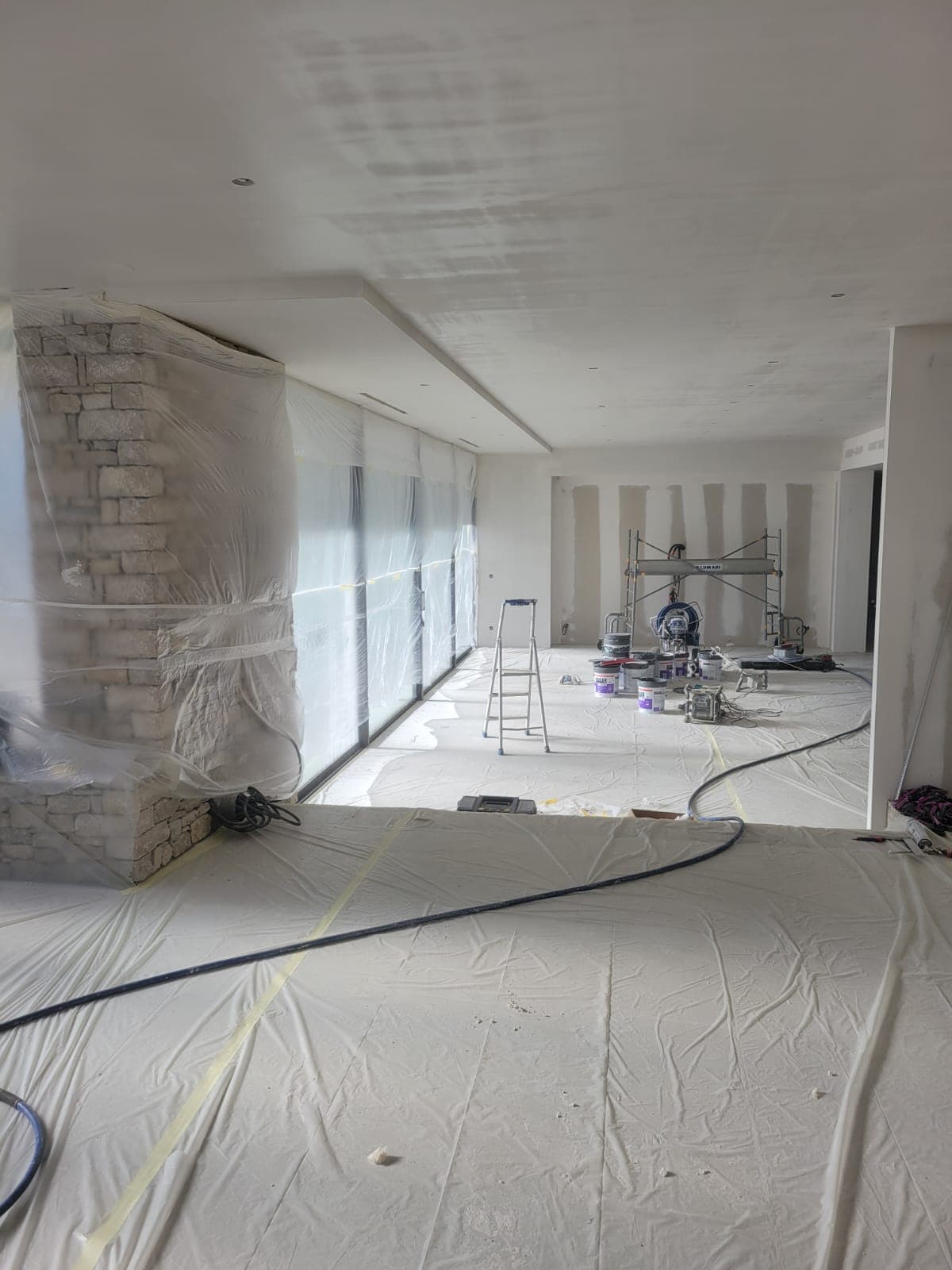 Mur en pierre et baies vitrées protégés par bâches avant peinture intérieure